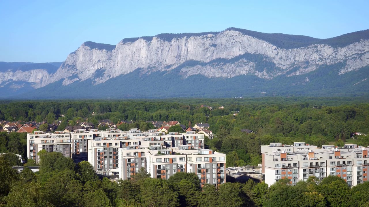 Ampia vista diurna che mostra moderni condomini bianchi con balconi in primo piano, una fascia continua di fitta foresta verde a metà strada e un.