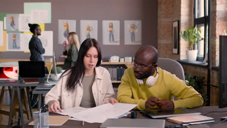 Man-And-Woman-Looking-At-Sketches-While-Sitting-At-Desk-In-An-Animation-Studio-1