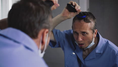 el médico corta el cabello en la cabeza con un cortador mirándose en el espejo