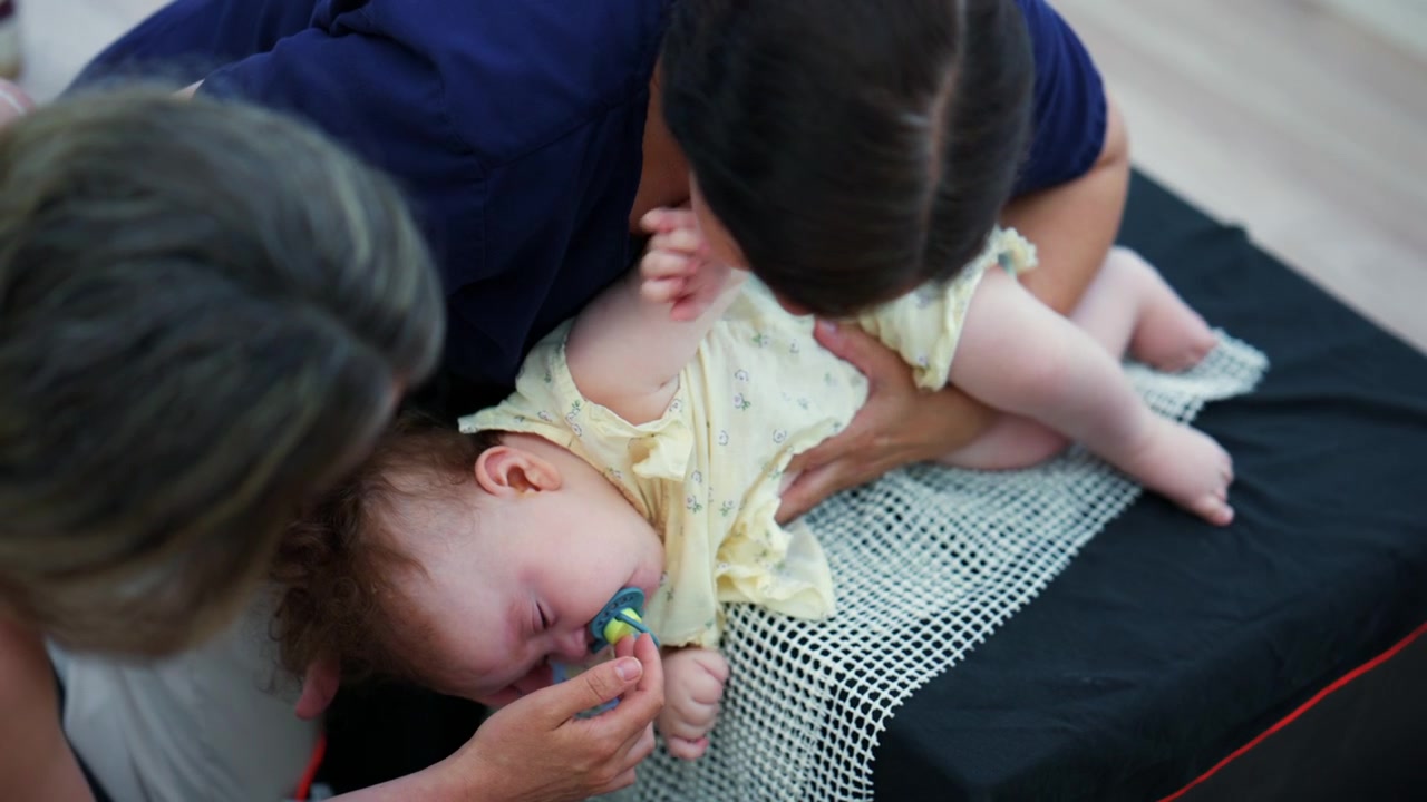 Un neonato tenuto in posizione verticale mentre un adulto gli sistema delicatamente il ciuccio, mostrando una scena di cura e legame familiare intimo.
