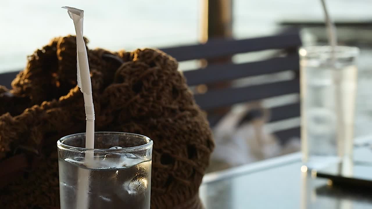 A refreshing iced beverage with a straw, set against a blurred outdoor background.