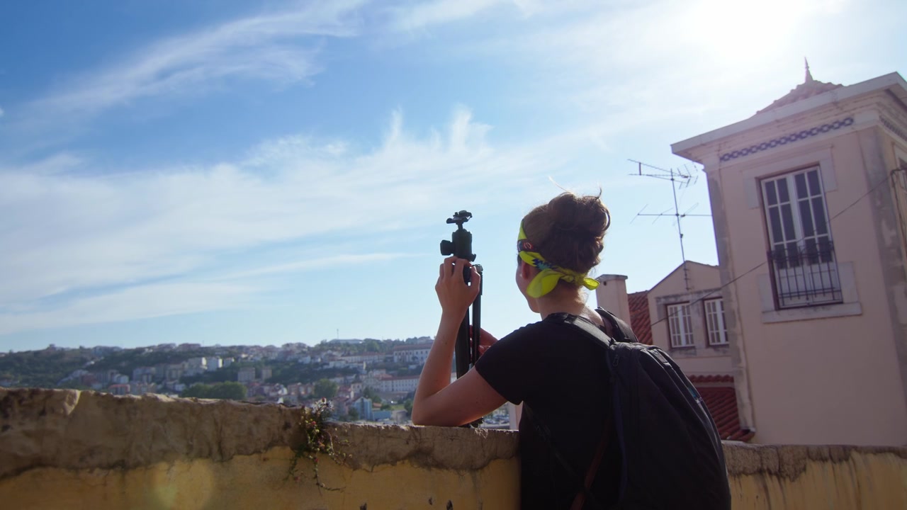 Ragazza con una fascia gialla per capelli, che tiene in mano un treppiede mentre ammira la vista panoramica del fiume Mondego a Coimbra, Portogallo