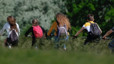 Kleine-Kinder-Radeln-Vorwärts-Auf-Einer-Landstraße-In-Der-Nähe-Mit-Riesigem-Gras-Und-Windigem-Tag