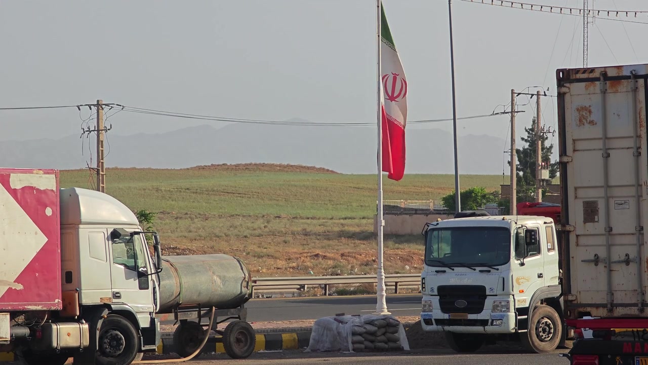 Bandiera iraniana che sventola vicino a un'autostrada trafficata con camion