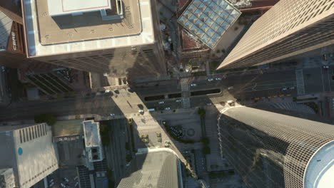 AERIAL:-Slow-uplifting-birds-eye-View-flight-over-Downtown-Los-Angeles-California-Grand-Avenue-in-beautiful-Sunrise-Light-with-view-of-skyscraper-rooftops-and-car-traffic-passing