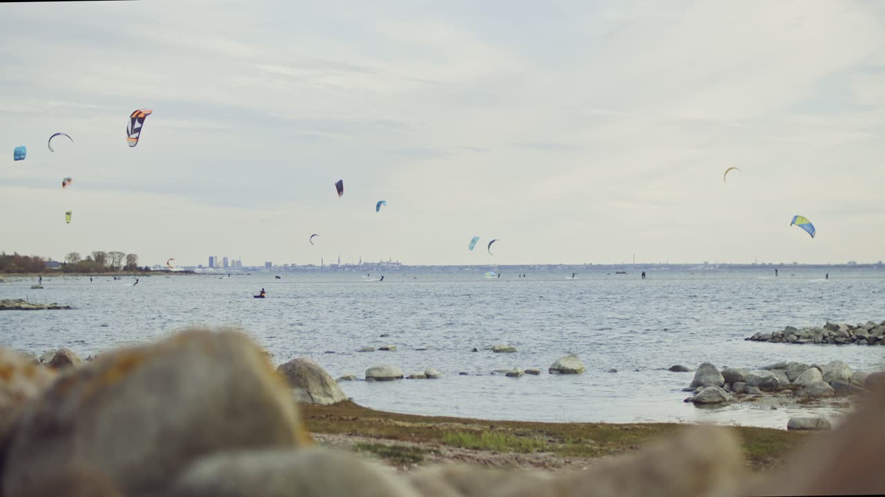las imágenes en cámara lenta capturan a hábiles kitesurfistas deslizándose a través de la pintoresca costa nórdica de estonia, enmarcada por la silueta icónica de la capital, tallin, en el fondo lejano
