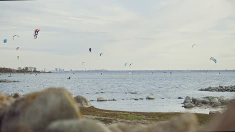 Slow-motion-footage-captures-skilled-kite-surfers-gliding-across-the-picturesque-Nordic-coastline-of-Estonia,-framed-by-the-iconic-silhouette-of-the-capital-city,-Tallinn,-in-the-distant-background