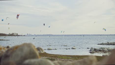 slow-motion footage captures skilled kite surfers gliding across the picturesque nordic coastline of estonia, framed by the iconic silhouette of the capital city, tallinn, in the distant background