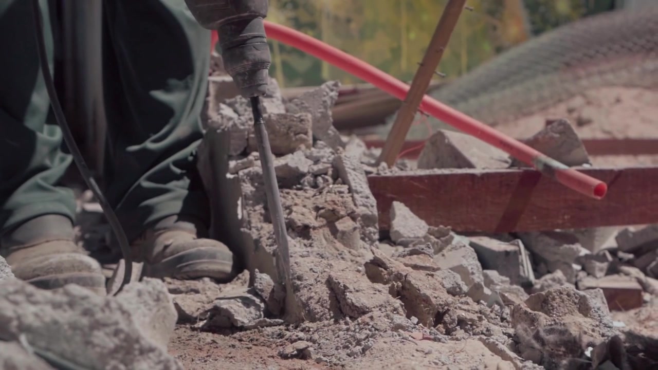 Operaio che rompe macerie di cemento con un attrezzo manuale durante la demolizione e la preparazione del cantiere, con detriti di muratura e materiali da costruzione sparsi nell'area di lavoro