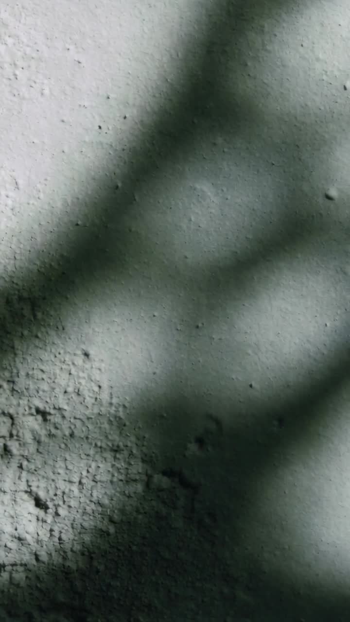 Vertical video: Shifting light moving curved shadows across interior plaster wall, revealing pits