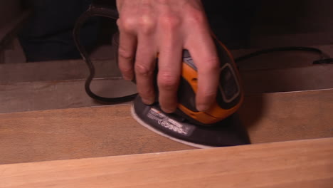 sanding a step on a wooden staircase with an electric tool