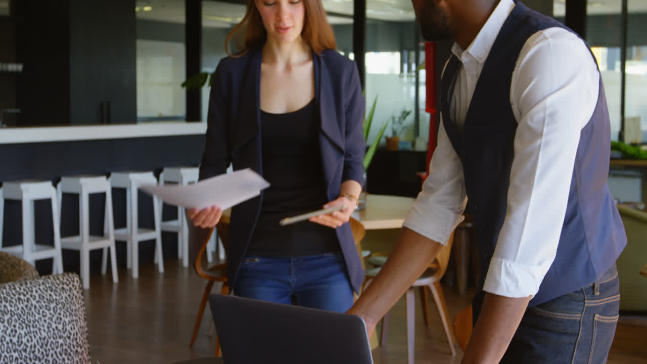 vista lateral de un joven empresario negro con una computadora portátil usando un teléfono móvil en una oficina moderna 4k