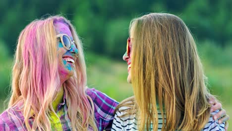 portrait shot of the cute and beautiful blonde girls in sunglasses smiling and laughing to the camera while posing at the holi fest celebration