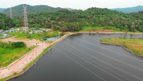 Cámara-De-Vista-De-Pájaro-Con-Disparo-De-Dron-En-órbita-Torre-De-Transmisión-Enrollada-Línea-Eléctrica-Junto-Al-Lago-Sobre-La-Montaña