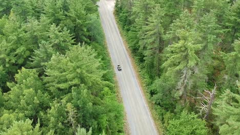 downwards tracking drone shot of someone driving an atv or four wheeler on a dirt road in the middle of the forest in canada