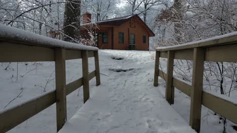 Zu-Fuß-über-Die-Brücke-In-Richtung-Kabine-In-Verschneiter-Winterlandschaft,-Vorwärtswagen