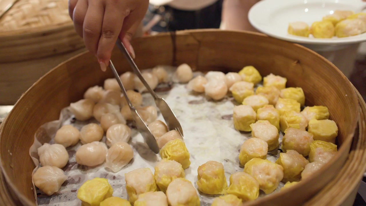 Una persona usa delle pinze di metallo per selezionare gnocchi di gamberi e maiale da una grande vaporiera