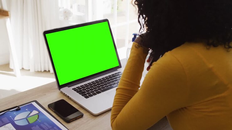 Vue de dos d'une femme afro-américaine regardant un ordinateur portable avec un écran vert, en télétravail.