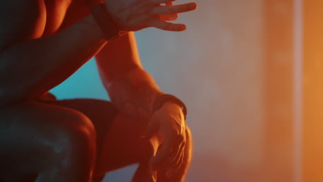 a tired athlete is resting in breathing heavily while sitting on a barbell in neon light after performing an exercise in slow motion. recuperate and prepare for a new breakthrough