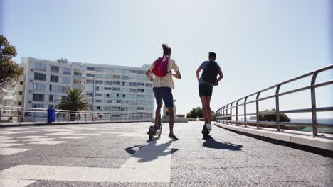 Happy-diverse-gay-male-couple-using-scooters-at-promenade-by-the-sea,-slow-motion