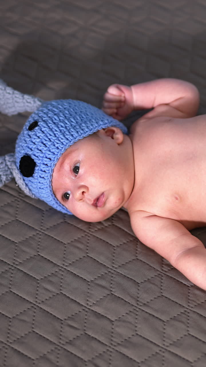 Sweet baby lying on the big bed in a costume of a puppy. Naked baby in the diaper and cap on the bed. View from above. Vertical video
