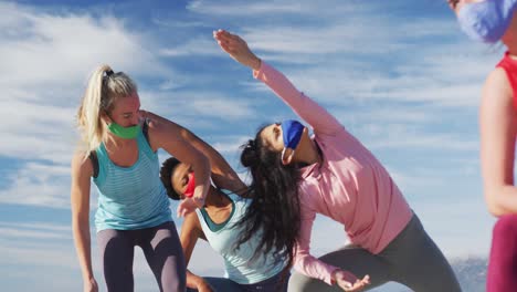 grupo de diversas amigas con máscaras faciales practicando yoga en la playa