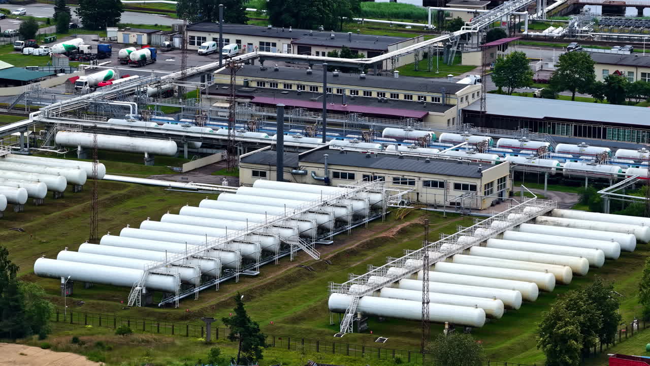 An aerial drone flies over a large industrial terminal in the Port of Riga, showing rows of horizontal bullet tanks used for the storage and transport of LPG and other pressurized gases