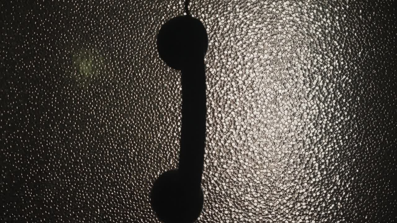 Phone Hangs by Cord in noir Room Silhouetted Against Textured Glass