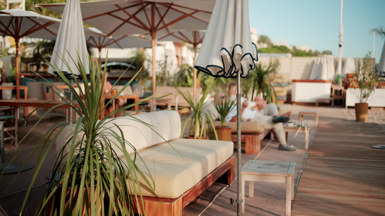 Cannes, France - October 13, 2025: People enjoying drinks and conversation at a stylish beach bar with large umbrellas and tropical plants