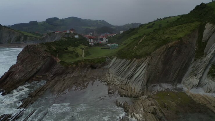 Panoramica aerea, stratigrafia flysch della scogliera della spiaggia di Itzurun e riflesso dell'acqua con cielo nuvoloso