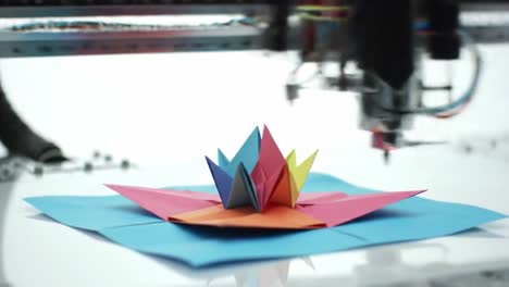 in a dynamic workshop, a cutting machine meticulously creates intricate paper designs. brightly colored sheets transform into a stunning pop-up structure, showcasing artistic innovation.