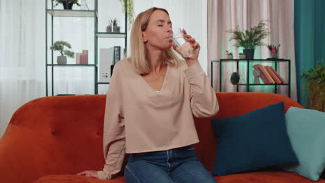 Thirsty-one-young-woman-sitting-at-home-holding-glass-of-natural-aqua-make-sips-drinking-still-water