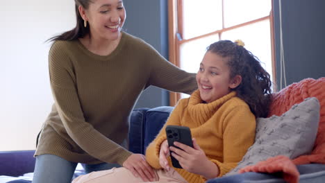 Feliz-Madre-E-Hija-Birraciales-Abrazándose-En-El-Sofá-Y-Usando-Un-Teléfono-Inteligente-En-Una-Soleada-Sala-De-Estar