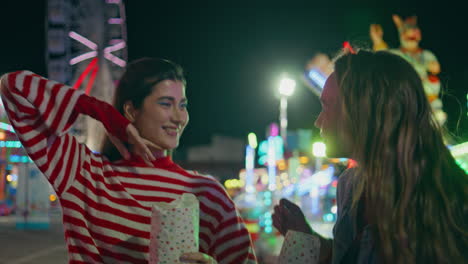 happy friends eating popcorn walking funfair closeup. joyful girls throw snacks