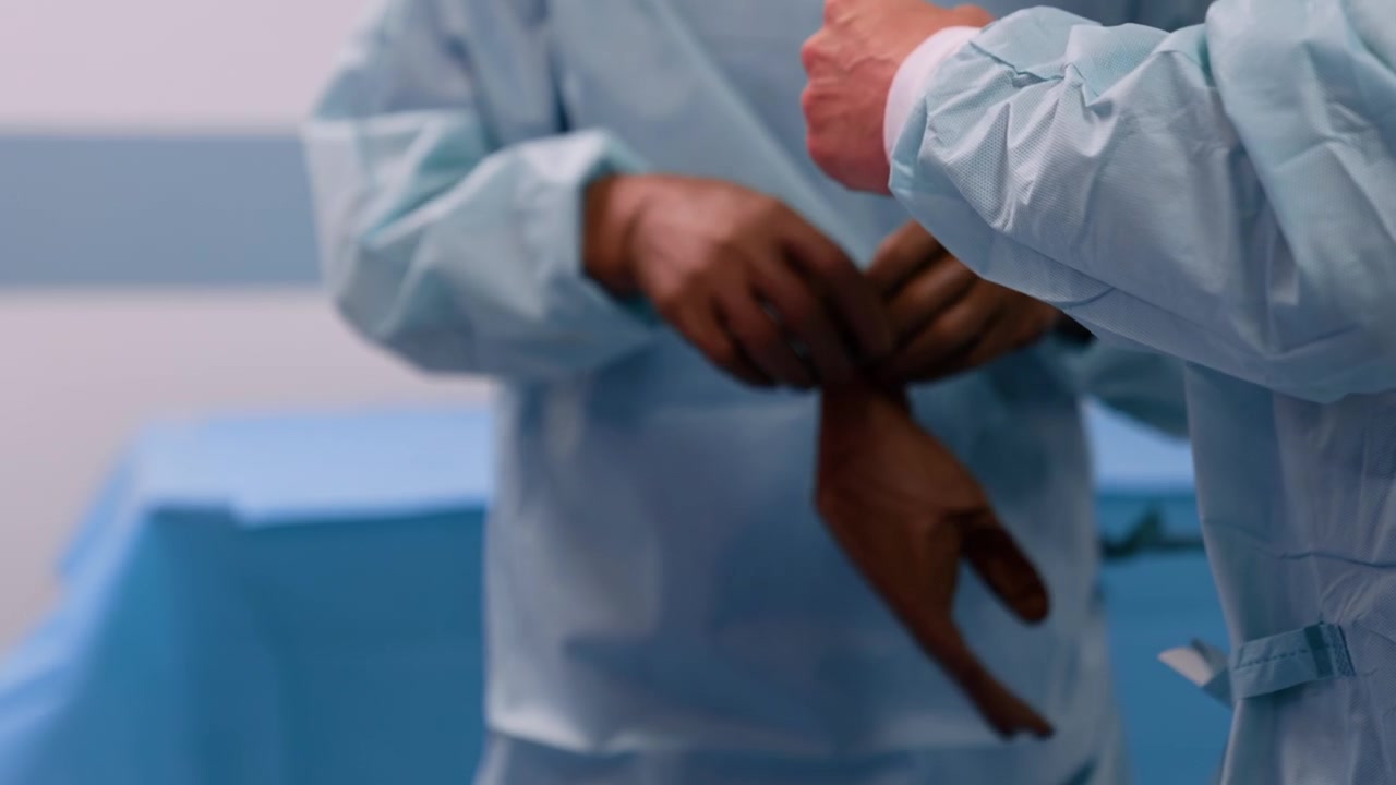 L'assistente aiuta il medico non riconoscibile a indossare i guanti in lattice. I chirurghi si preparano per l'operazione
