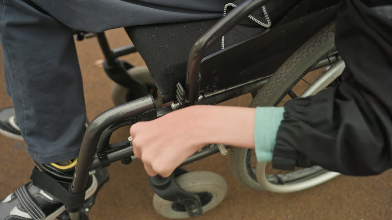 Youth Maneuvers Mobility Device Outdoors, Young Person Navigates Park Pathway Independently, Teenage Individual Operating Wheelchair With Skill Along Green Park Trail While Maintaining Focus