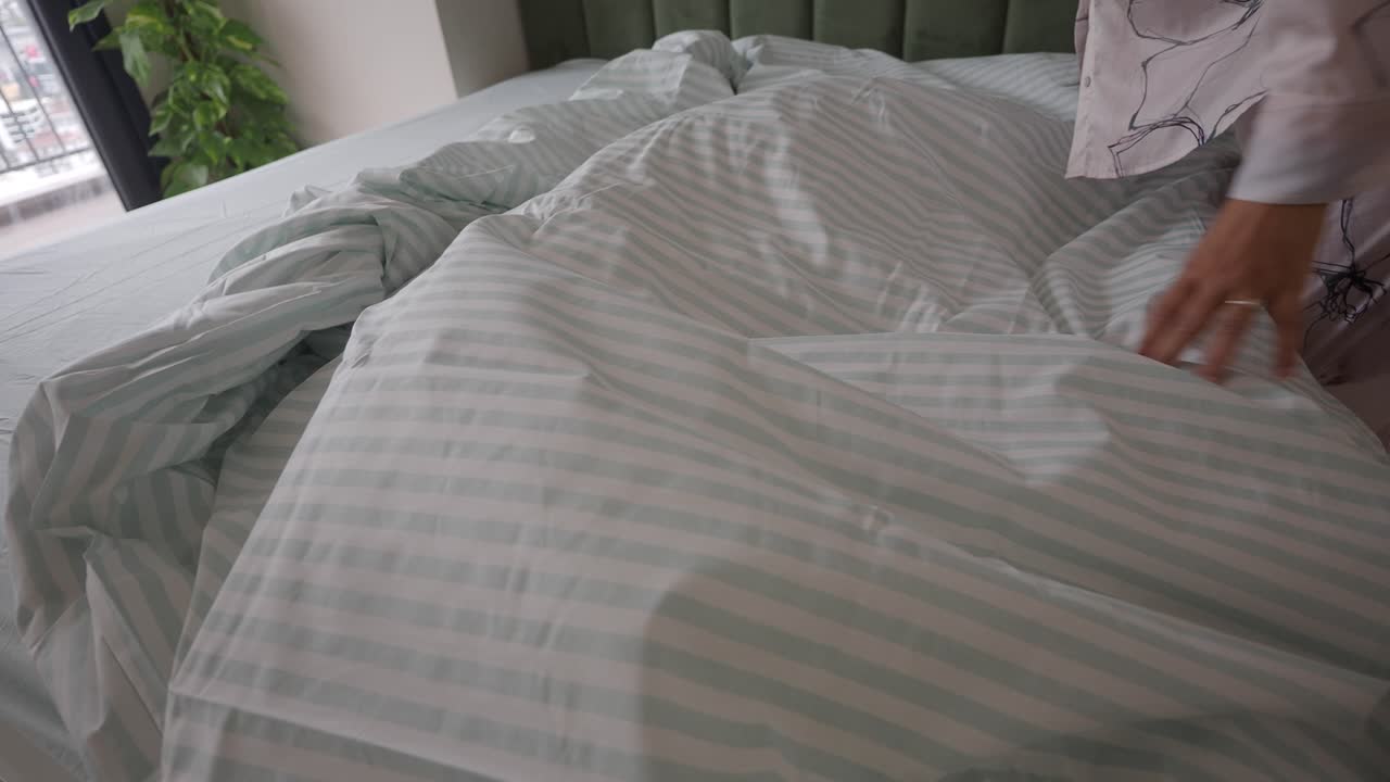 Seseorang merapikan tempat tidur dan memasang sarung selimut bergaris.