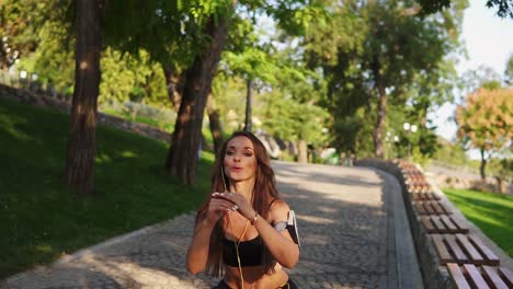 mujer joven haciendo sentadillas en el parque escuchando la música, respirando lentamente y mirando a la cámara. disparo en cámara lenta