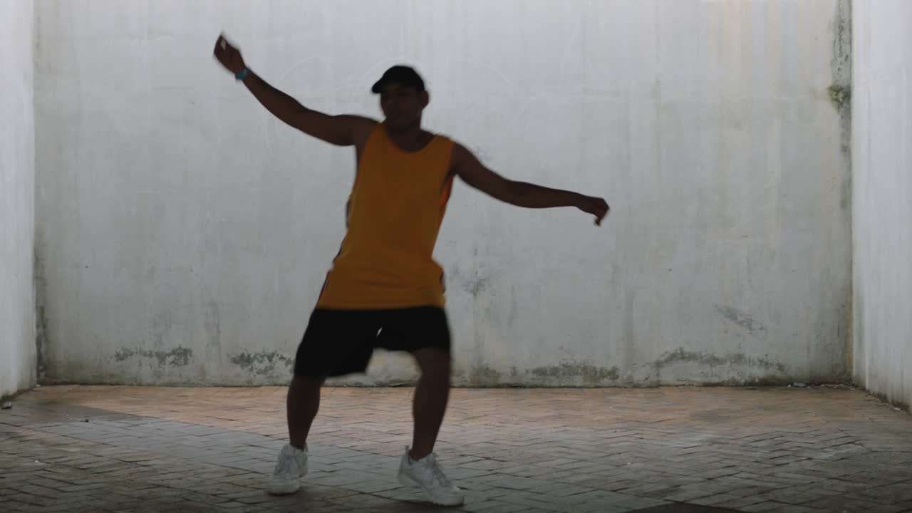 hombre bailarín joven bailarín de calle feliz realizando varios movimientos de baile de estilo libre adecuado hombre de raza mixta practicando en un almacén grungy con chaleco amarillo