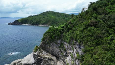 Rising-Overhead-Drone-Shot-of-Tropical-Island-Coastline-with-lush-rainforest,-idyllic-sand-beach,-and-rock-formation-from-recumbent-fold