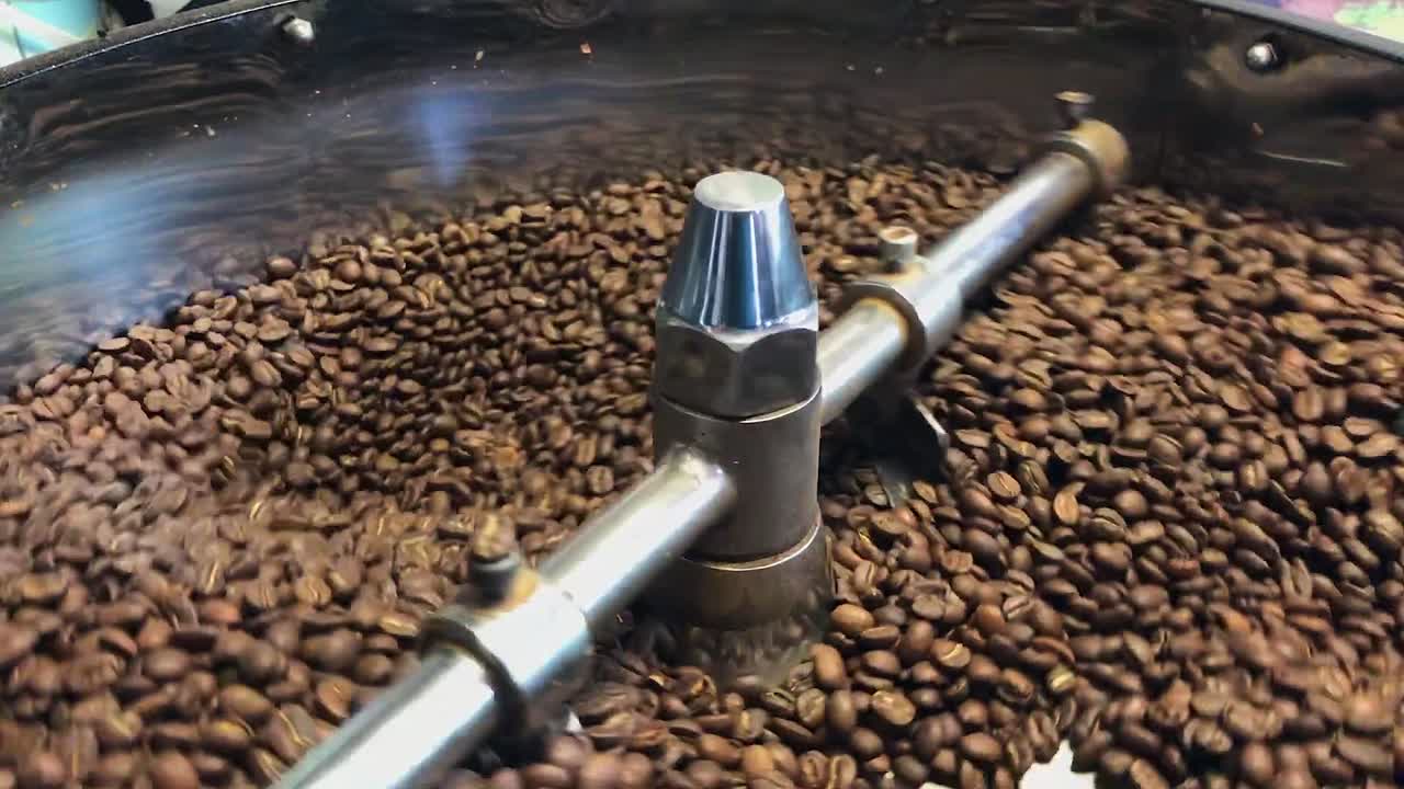 Grãos de café secos e marrons torram em torrador de aço inoxidável, agitados por pá