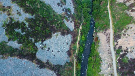 top down forward moving aerial view of wninding river with scattered rocks on hillside with hiking path. aerial view of british countryside