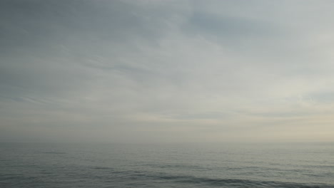 Wavy-ocean-water-waves-of-Malibu,-on-a-dull-cloudy-day-evening-with-passing-clouds