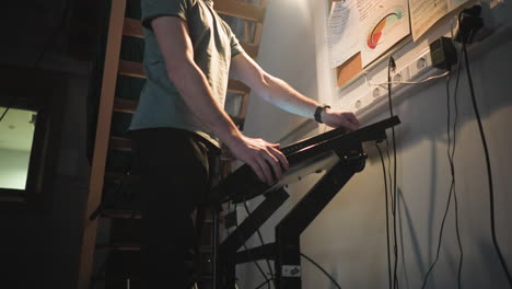 man walks through backstage area in dim lighting near control panel and corkboard covered with notes and charts. industrial environment with visible cables, stairs, and power outlets