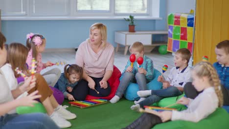 children enjoying a music lesson in classroom with female teacher, kids with down syndrome and healthy children play on maracas, xylophones and bells