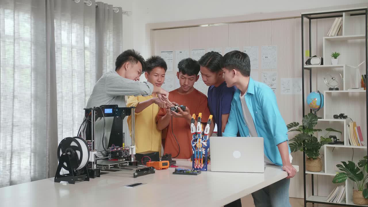 사이보그 손과 3d 프린팅을 가진 젊은 아시아 소년 그룹이 집에서 노트북을 작업하는 동안 회로판을 고치고 있습니다.