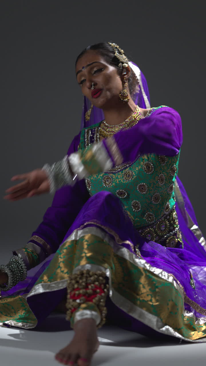 video vertical de una bailarina de kathak femenina realizando un baile vestida con un vestido tradicional indio sentada en el suelo en el centro de atención 3