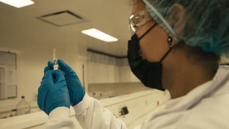 female scientist in mask wearing glasses checking test tube while working in research laboratory