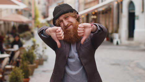 Upset young man showing thumbs down sign disapproval dissatisfied bad work mistake in city