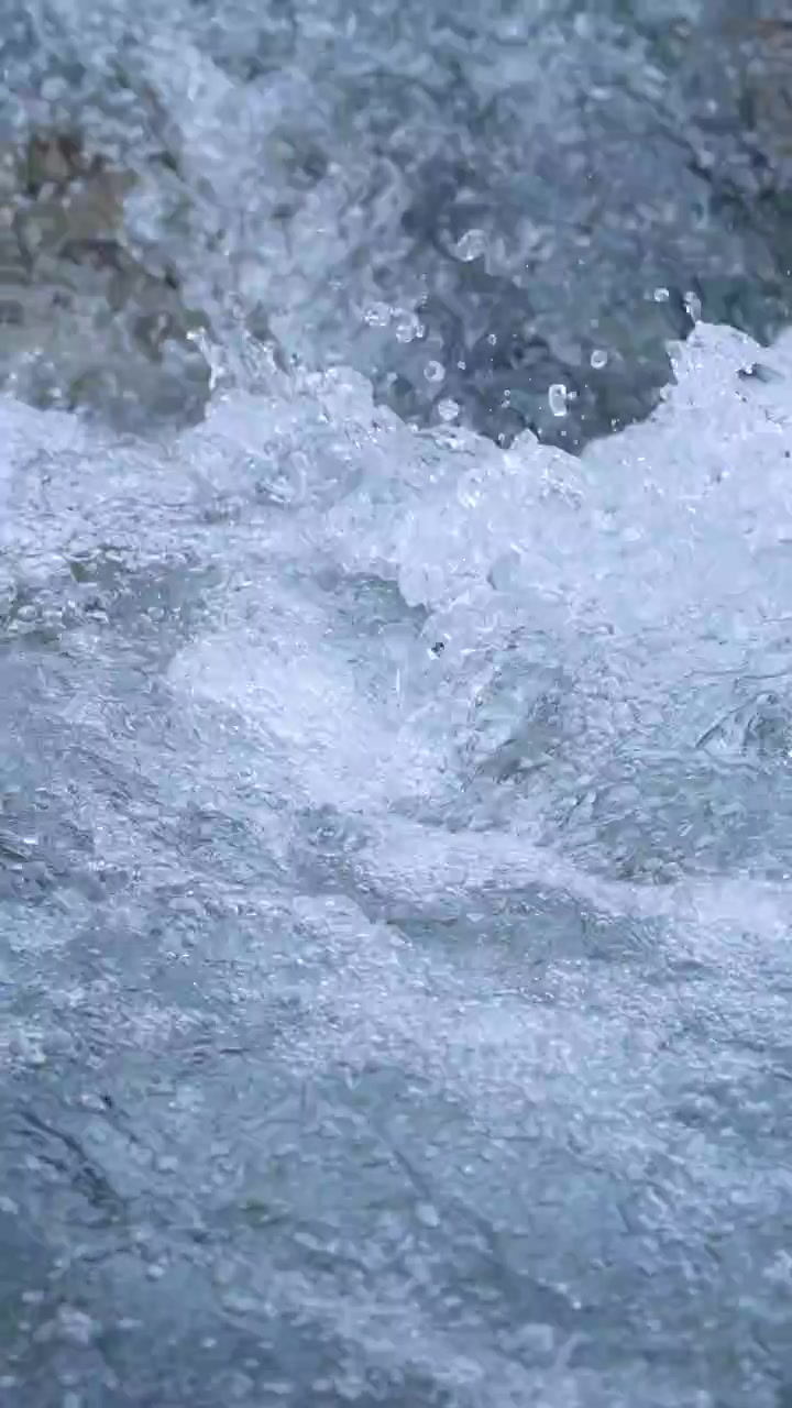 Acqua limpida di ruscello di montagna scorre energicamente su rocce lisce alla luce del giorno, con schizzi dinamici, bolle e texture dettagliate catturati in primi piani stabili.